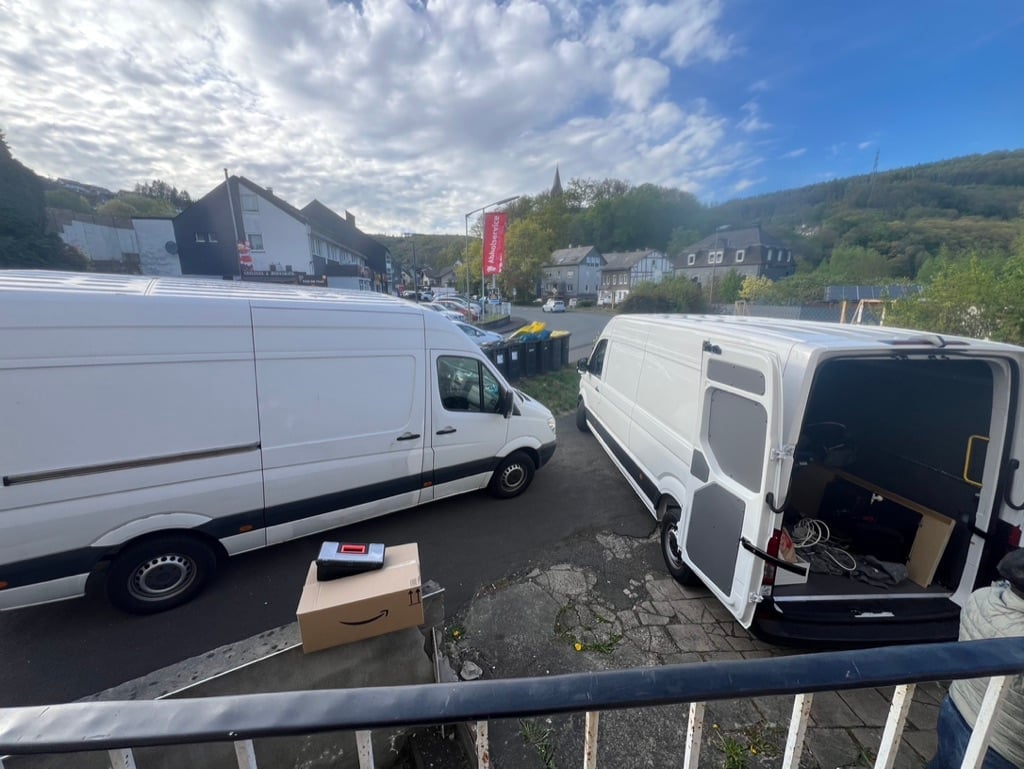 Two white commercial vans parked on a street with a cardboard box in the foreground, mountains and town visible in the background