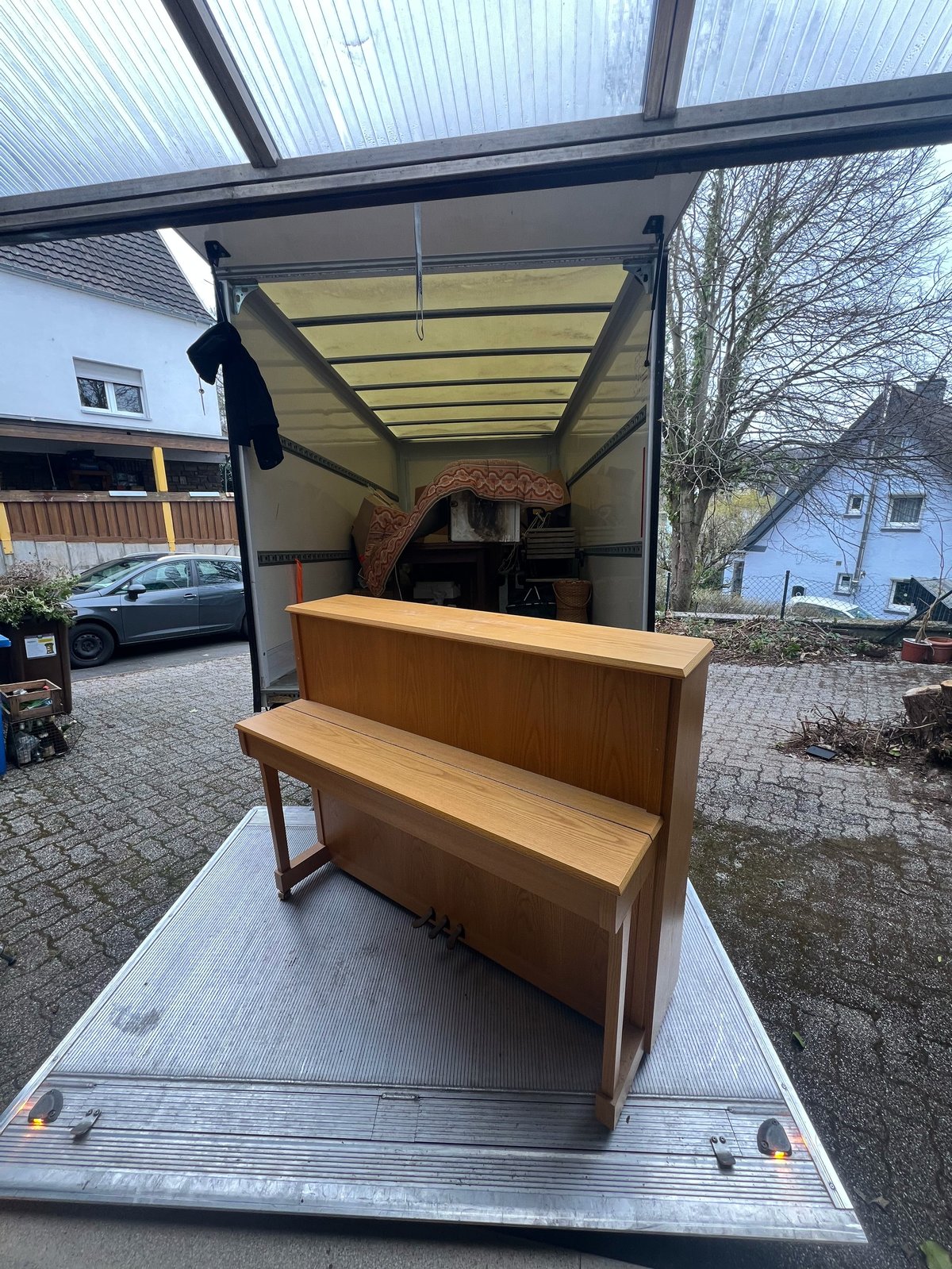 Wooden piano being loaded into a moving truck on a residential driveway