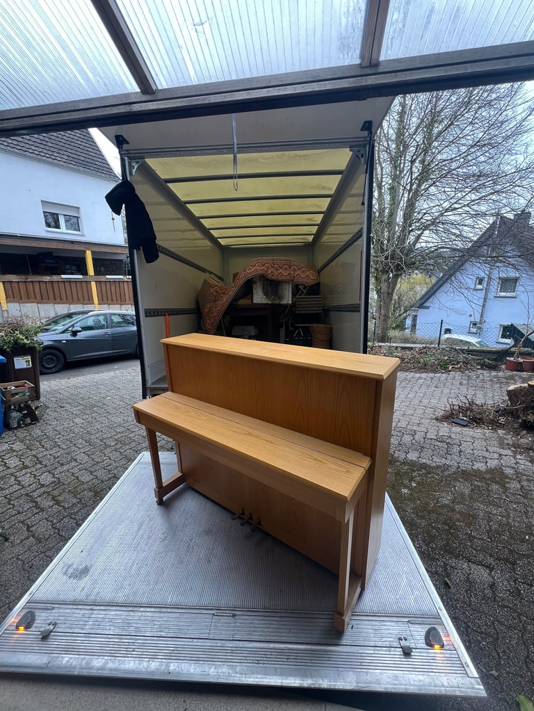 Wooden piano being loaded into a moving truck on a residential driveway